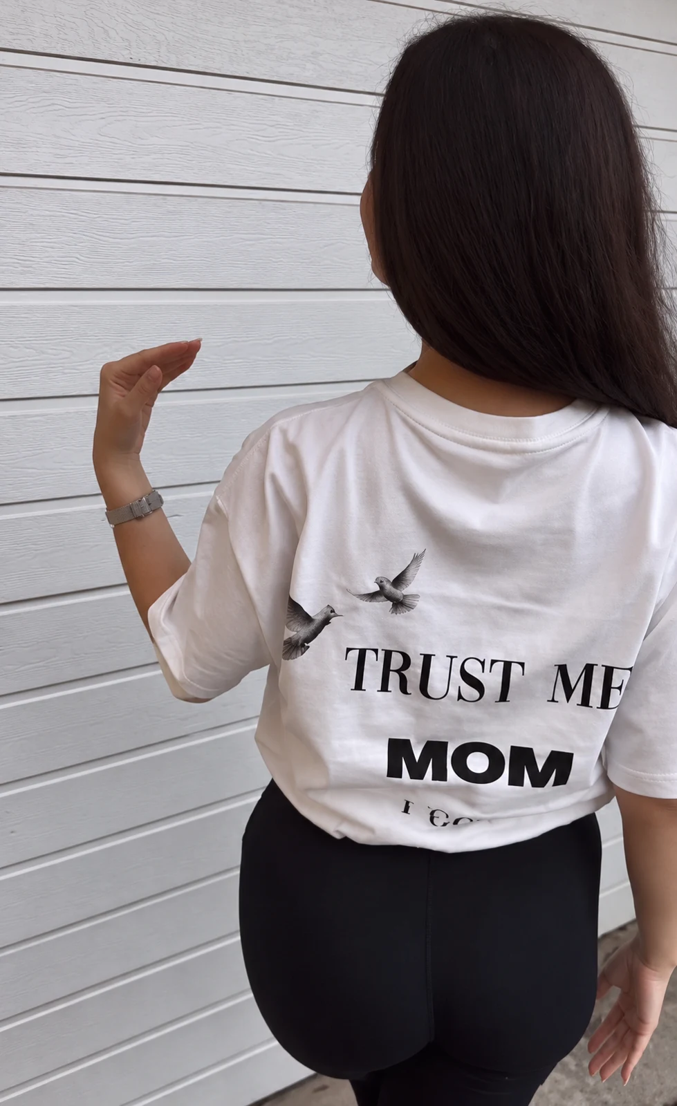 Weißes TRUST ME MOM Shirt vor einer Holzwand